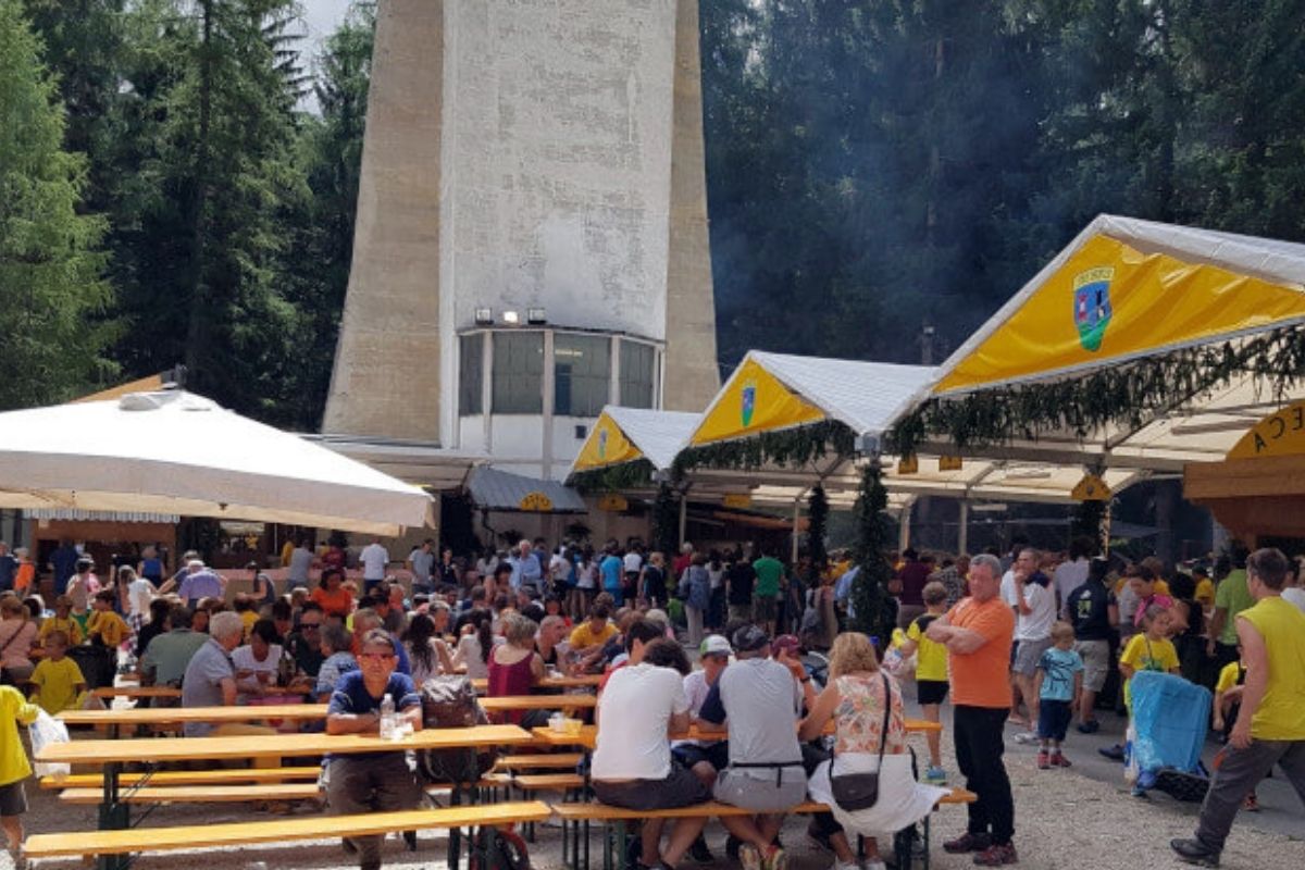 Sagra all'aperto a Cortina d'Ampezzo, tavolate di legno, gente che mangia piatti tipici, band musicale e montagne sullo sfondo